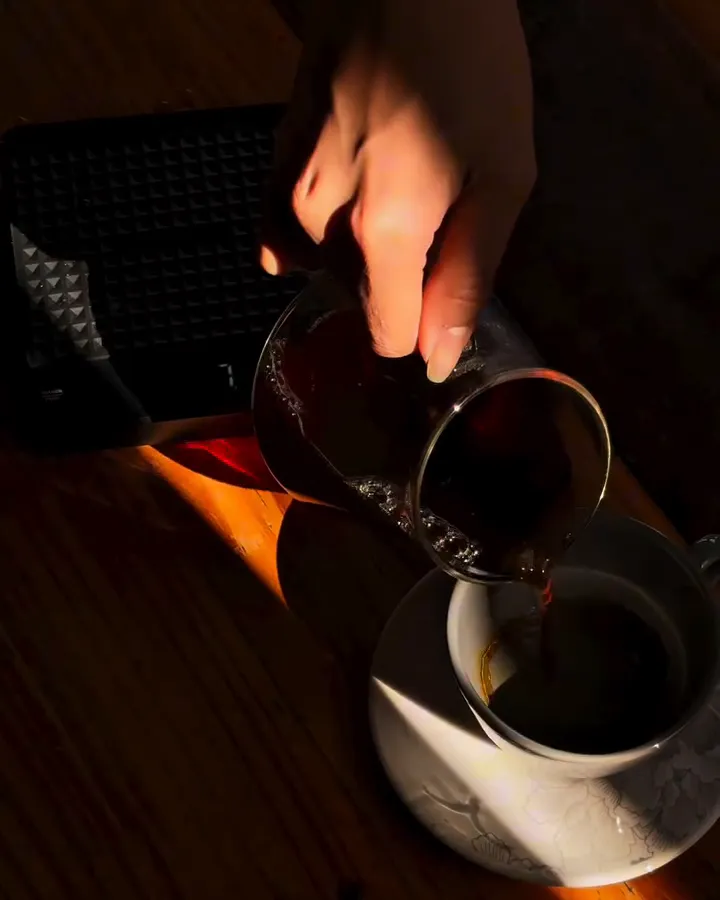Café coado sendo servido da jarra de vidro numa xícara branca, sob luz de fim de tarde.